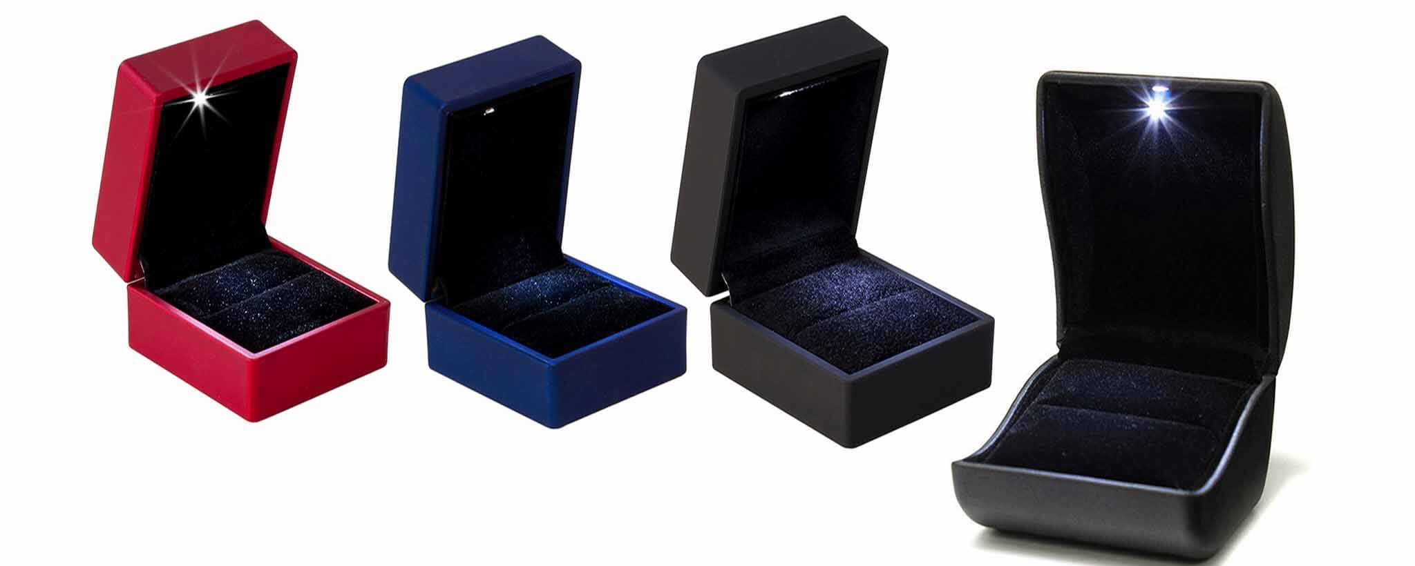 Four open jewelry boxes in red, blue, black, and dark gray on a white background.